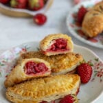 Strawberry Hand Pies on a dessert plate with fresh strawberries and another plate of hand pies in the background.