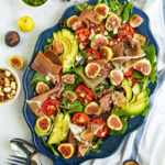 Salad with fresh figs, prosciutto, tomatoes, avocado and fresh greens on a blue platter