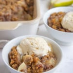 Pear Crisp in a white bowl and topped with a scoop of vanilla ice cream.