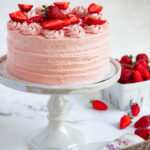 Fresh Strawberry Cake on a cake stand next to a basket of fresh strawberries