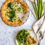 Asparagus and Leek Quiche in a ceramic pie dish with a slice on a salad plate with a small green salad