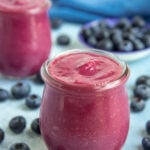 Blueberry curd in two small jars surrounded by blueberries