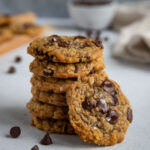 A stack of six oatmeal chocolate chip cookies with one cookie leaning against the stack of cookies
