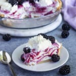 A slice of blackberry ice cream pie on a dessert plate with the rest of the pie and a bowl of blackberries in the background