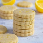 A stack of 6 lemon shortbread cookies surrounded by cookies and fresh lemon