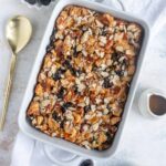 prune bread pudding in a white baking dish with a small container of bourbon whiskey sauce next to the baking dish