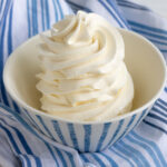a swirl of Swiss meringue buttercream in a blue-striped bowl with a blue tea towel in the background