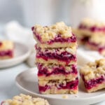 a stack of 4 cherry pie bars with more cherry pie bars on a board in the background