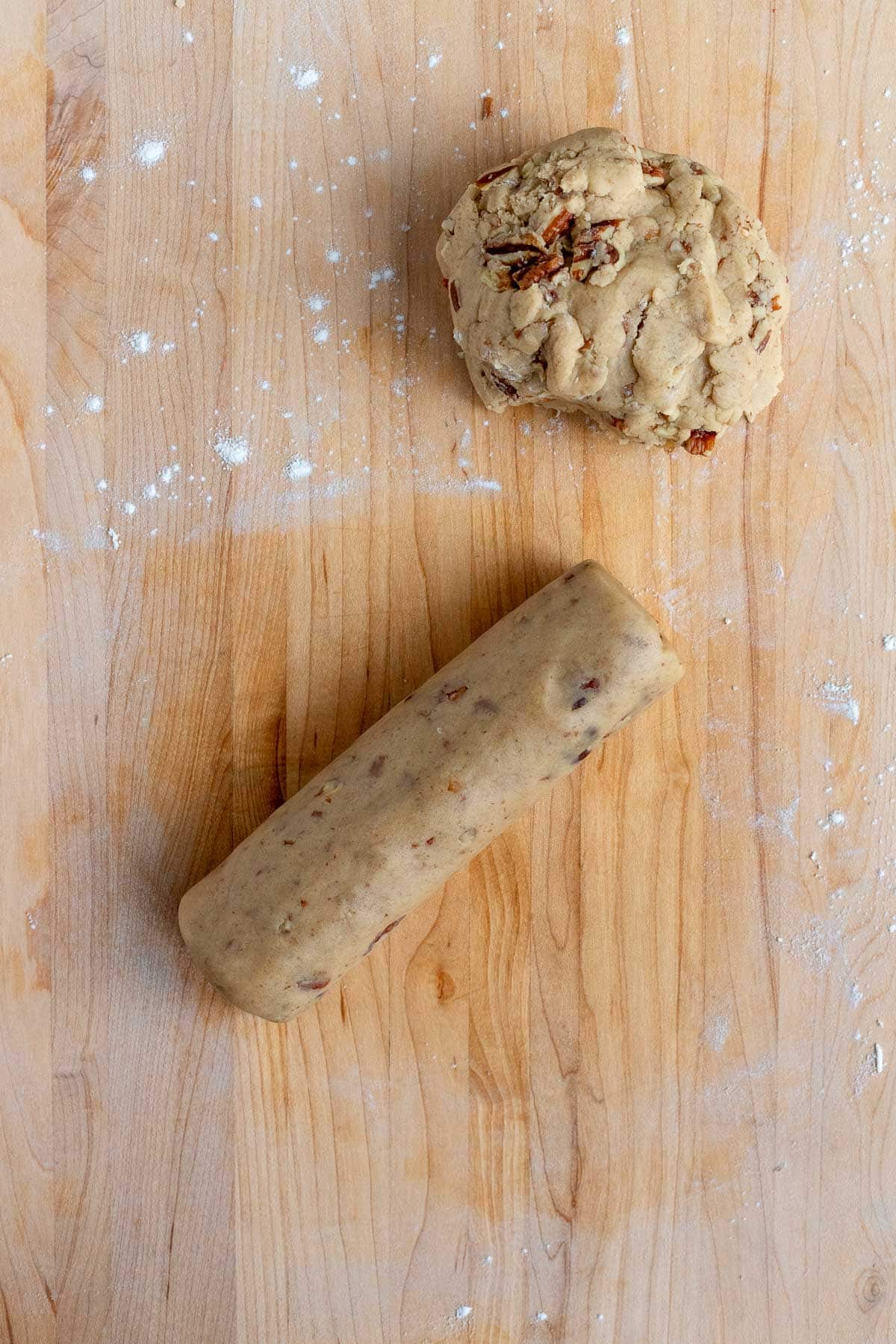 One half of the cookie dough is in a ball of dough. The other half of dough is rolled into a short cookie dough log. Both pieces are on a wooden board.