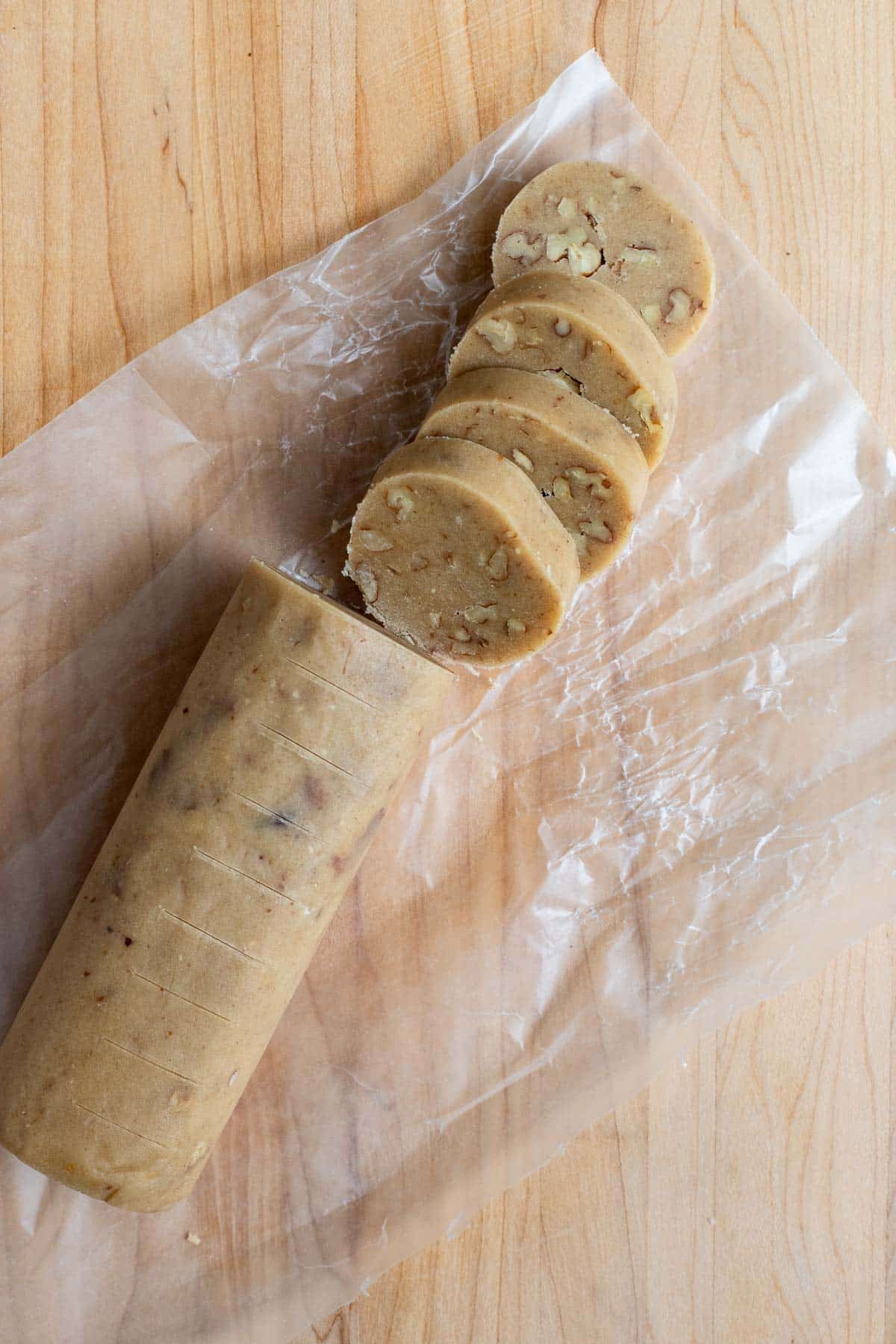 Unwrapped brown sugar pecan cookie dough log cut into 1/2-inch slices. The sliced cookies are leaning against each other