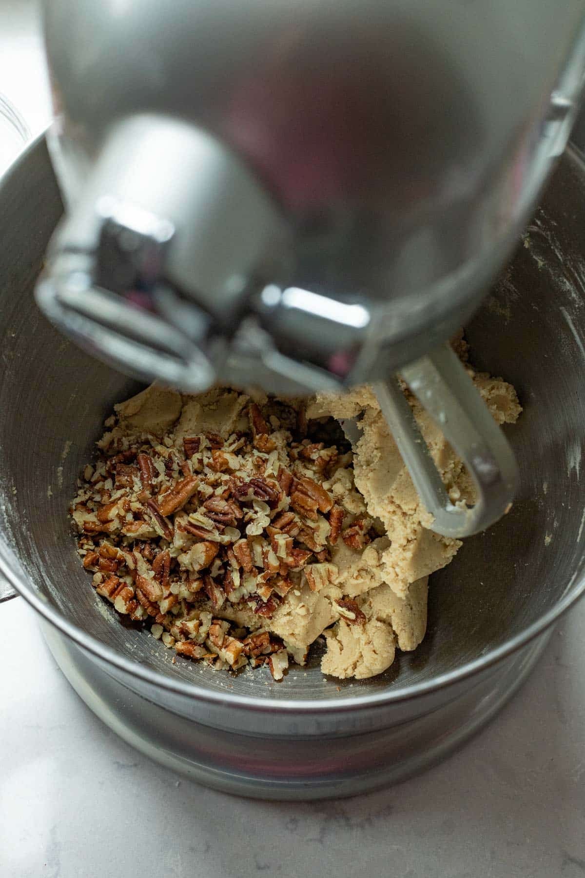 The chopped pecans added to the brown sugar cookie dough in the bowl of a stand mixer