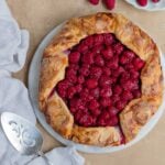 A raspberry galette on a white plate with a small plate of fresh raspberries next to the galette