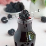 Blackberry simple syrup in a small glass jar with a blackberry suspended on top.