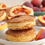 A small stack of peach hand pies. The one on top is cut in half exposing the peach filling