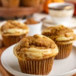 Two pumpkin cream cheese swirl muffins on a small plate with more muffins in the background