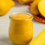 Mango curd in a pint jar with whole champaign mangos in the background