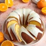 An orange pound cake with an orange glaze on a white serving platter. There are 4 slices cut and arranged on the platter