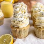 6 Lemon poppy seed cupcakes with lemon buttercream arranged in two rows on a wood board. A small jar of lemon curd is in the background.