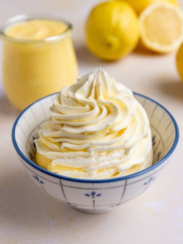 Lemon Swiss meringue buttercream in a small bowl with a blue pattern. Fresh lemons are in the background