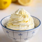 Lemon Swiss meringue buttercream in a small bowl with a blue pattern. Fresh lemons are in the background