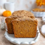 Sliced banana pumpkin bread on a white platter. The banana pumpkin bread is deep golden orange color and has a lighter color crumble on top