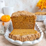 Banana pumpkin bread loaf on a white ceramic platter. The loaf is sliced and one sliced is laying on the platter