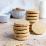 Two stacks of brown sugar shortbread cookies with a glass of milk in the background.