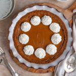 Baked sweet potato pie decorated with swirls of whipped cream.