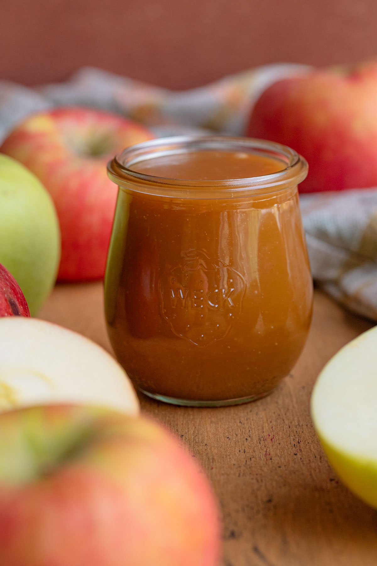 An 8-ounce jar filled to the top with apple caramel cider sauce.  The jar is surrounded by fresh apples
