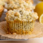 Lemon poppy seed muffin on a wire rack. The liner paper is peeled down and you see the ridges left behind by the paper liner. The crumble topping is toasted around the edges.