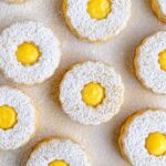 Lemon curd sandwich cookies with lemon curd in the center. The top of the cookies have a sprinkle of powdered sugar