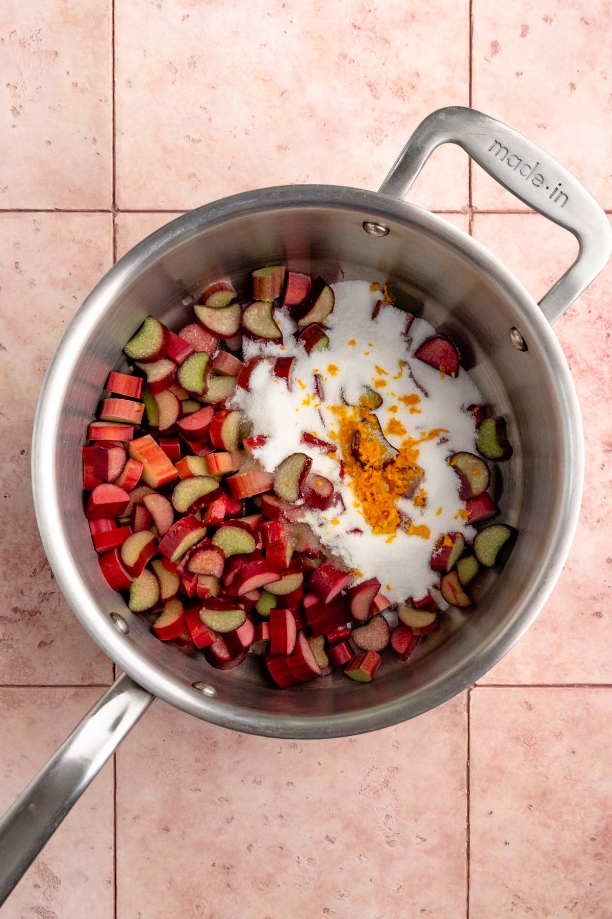 Chopped rhubarb, sugar, orange zest, and orange juice in a stainless steel plan