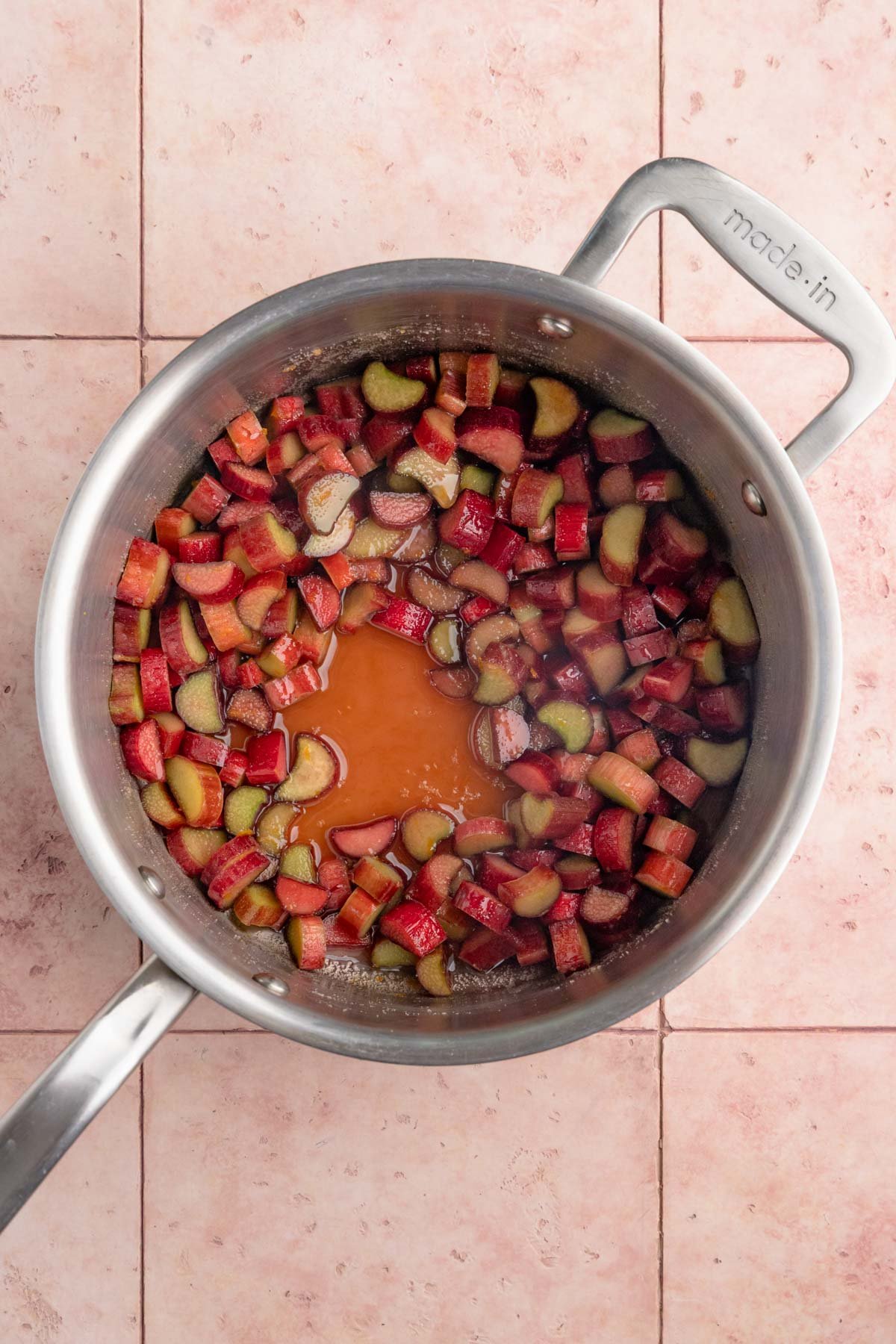 Macerated rhubarb in stainless steel pan. There is liquid on the bottom of the pan