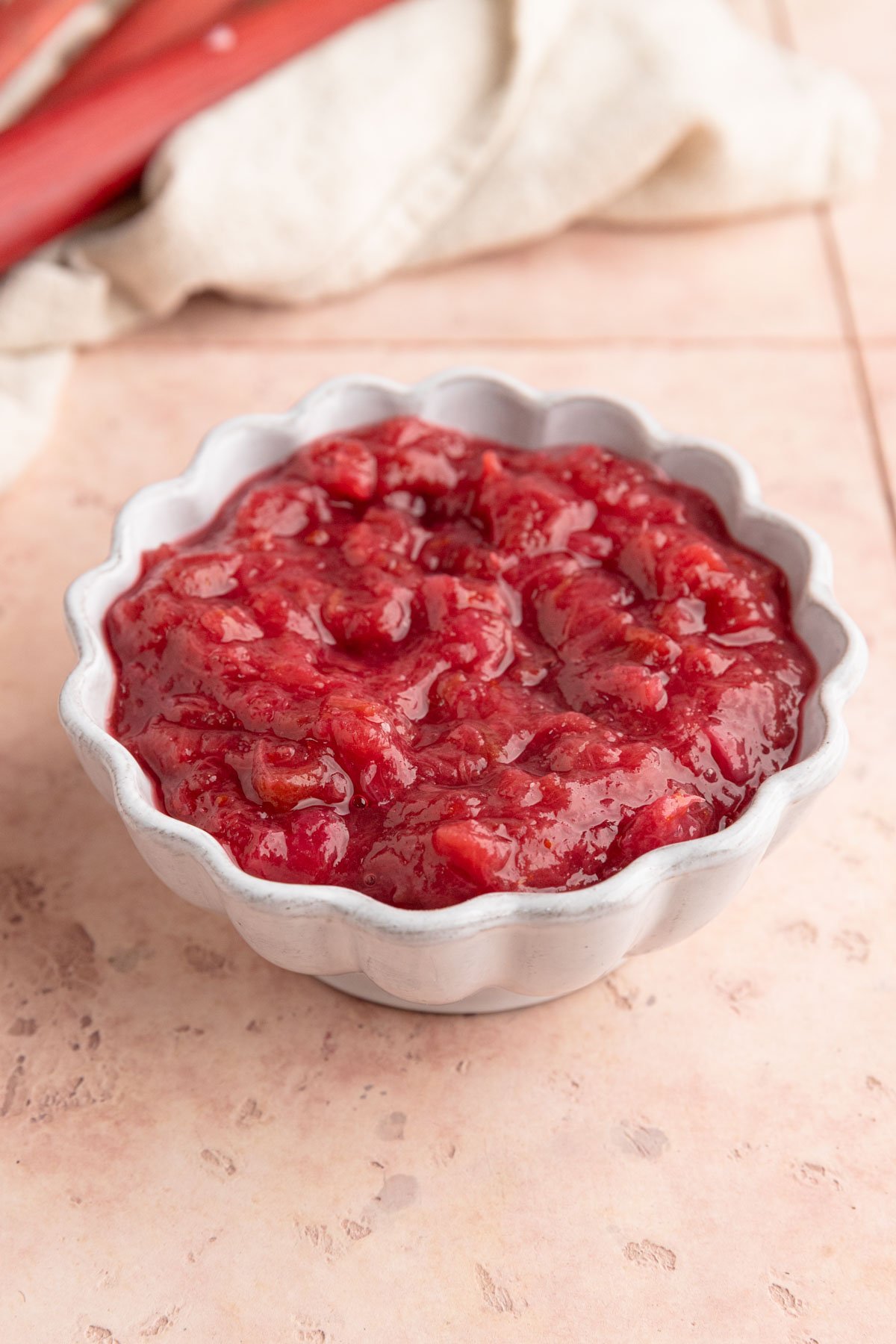 Rhubarb compote in a white ceramic bowl in fresh rhubarb in the background
