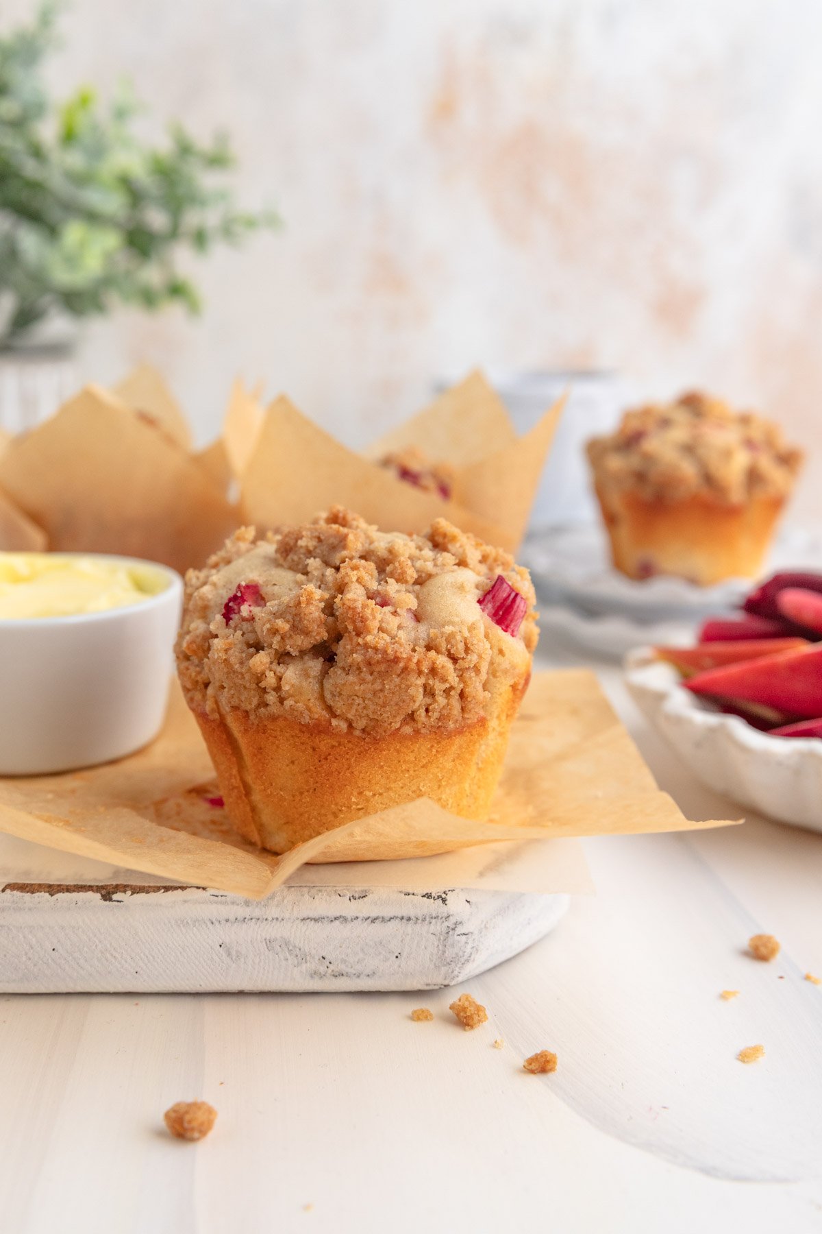 rhubarb muffin on a piece of brown parchment paper with a small dish of butter to the left and more muffins in the background