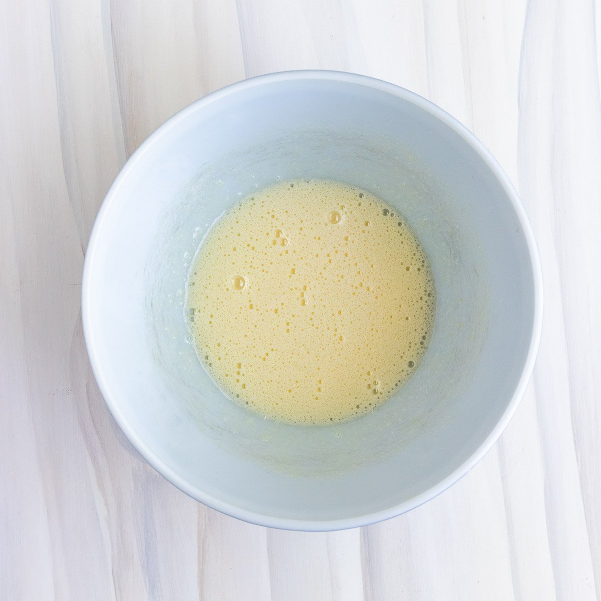 Egg and sugar whisked together in a white ceramic bowl