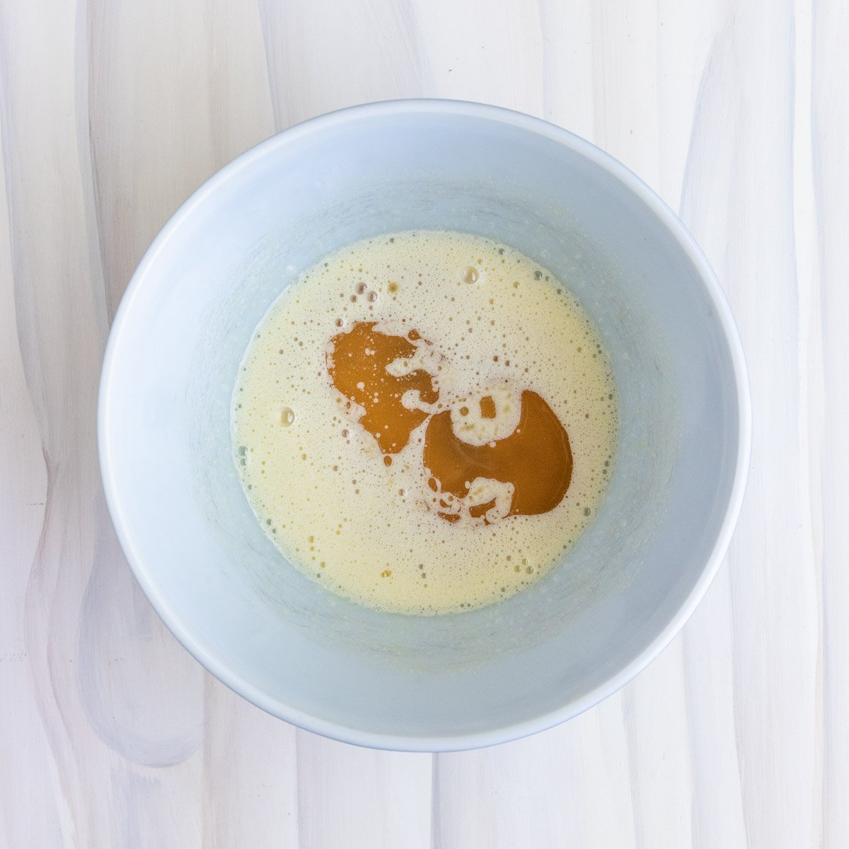 melted butter added to sugar and egg mixture in a white ceramic bowl