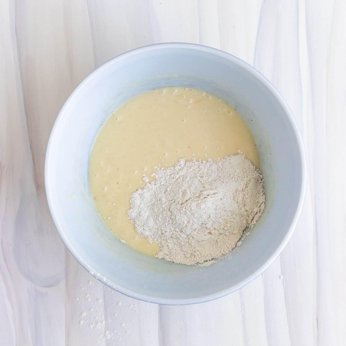 flour mixture added to the muffin batter in a white ceramic bowl