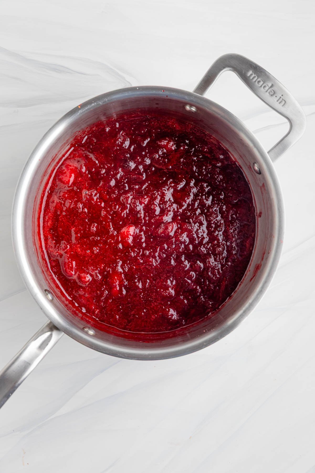 A top down view of cooked strawberry rhubarb jam in a stainless steel sauce pan