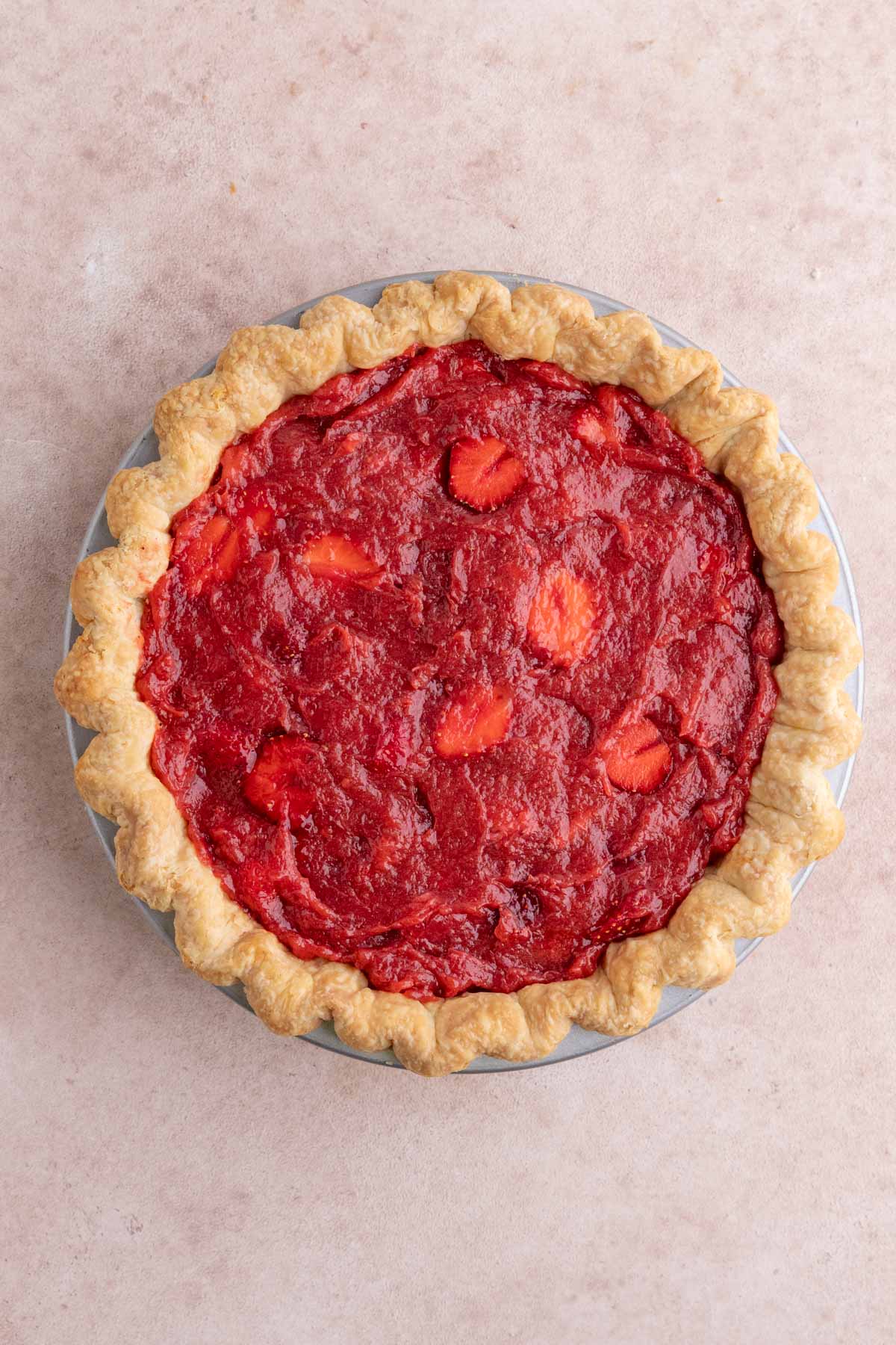 Flaky brown pie crust filled with bright red cooked strawberry rhubarb filling and fresh strawberries