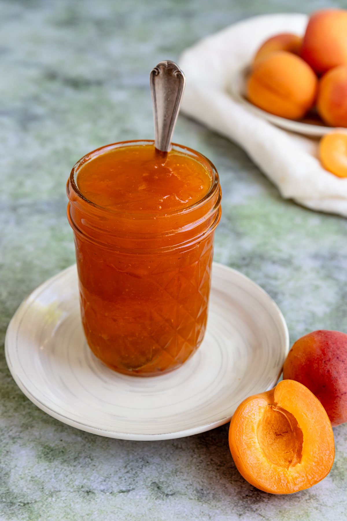 A pint jar filled with apricot jam and a spoon sticking out of the jar.  The jar sits on a small white plate