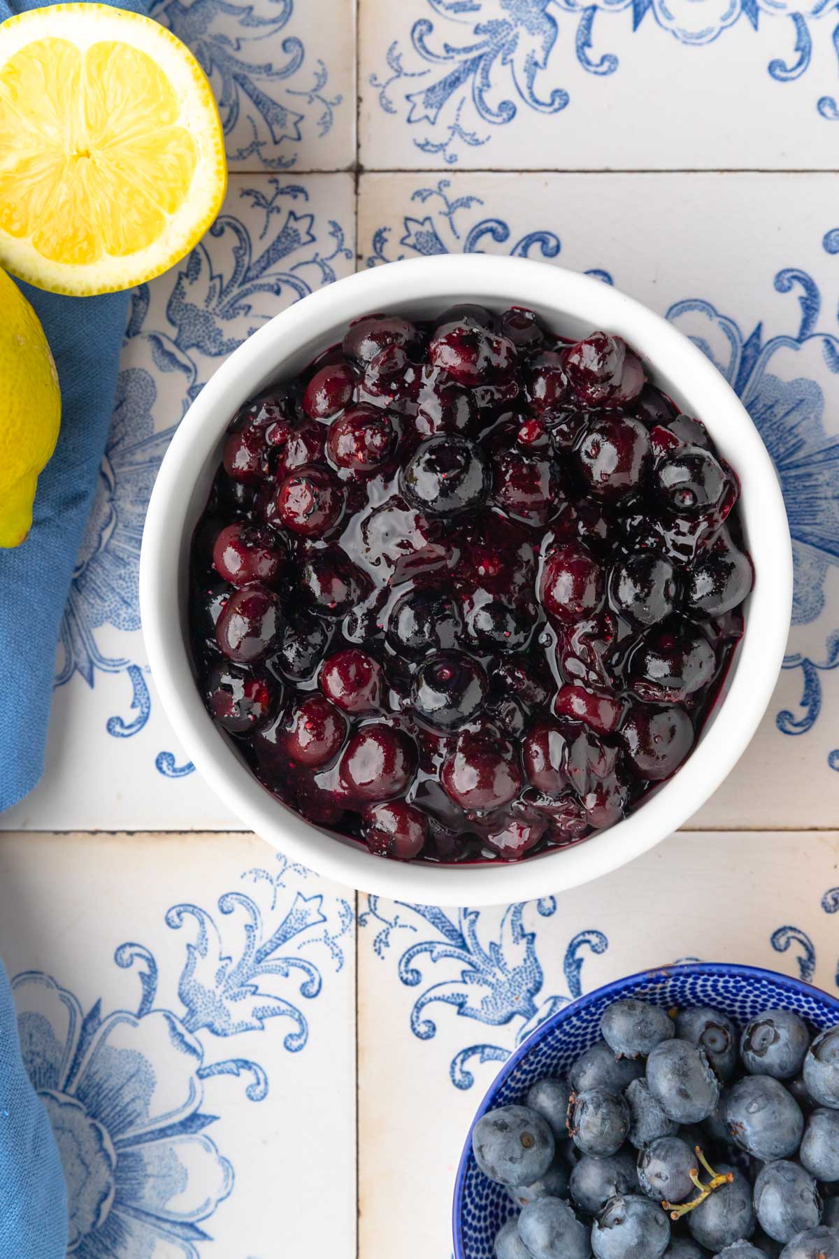 Blueberry compote in a white bowl, next to a bowl with fresh blueberries