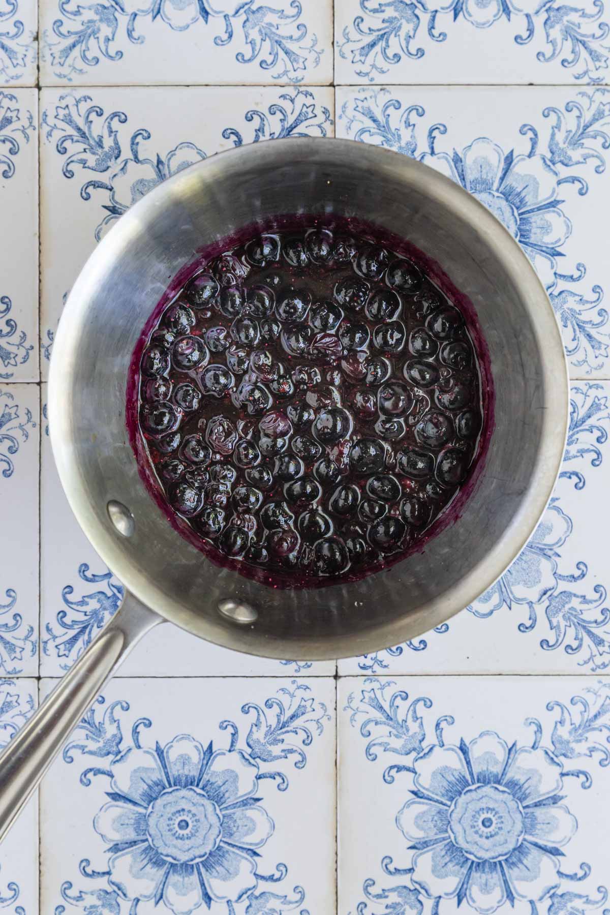 Cooked blueberry compotes in a stainless steel pan. The berries have turned purple