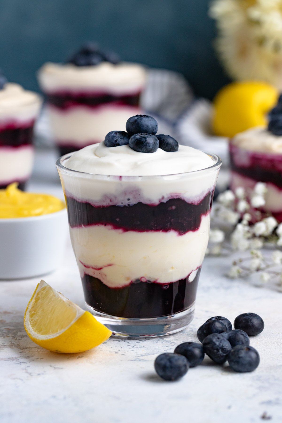 Blueberry lemon parfait in a glass jar. There are 2 layers of blueberry compote with a layer of lemon cream in between. The dessert is topped with whipped cream and fresh blueberries.