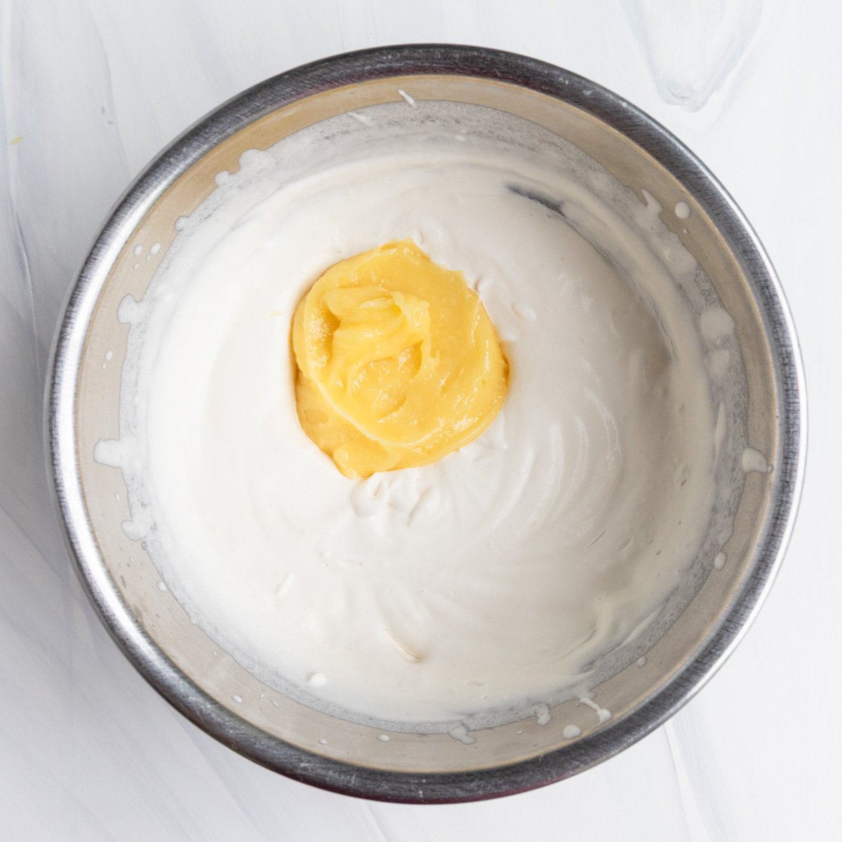 A stainless steel bowl with whipped cream and a 1/2 cup of lemon curd added to the bowl