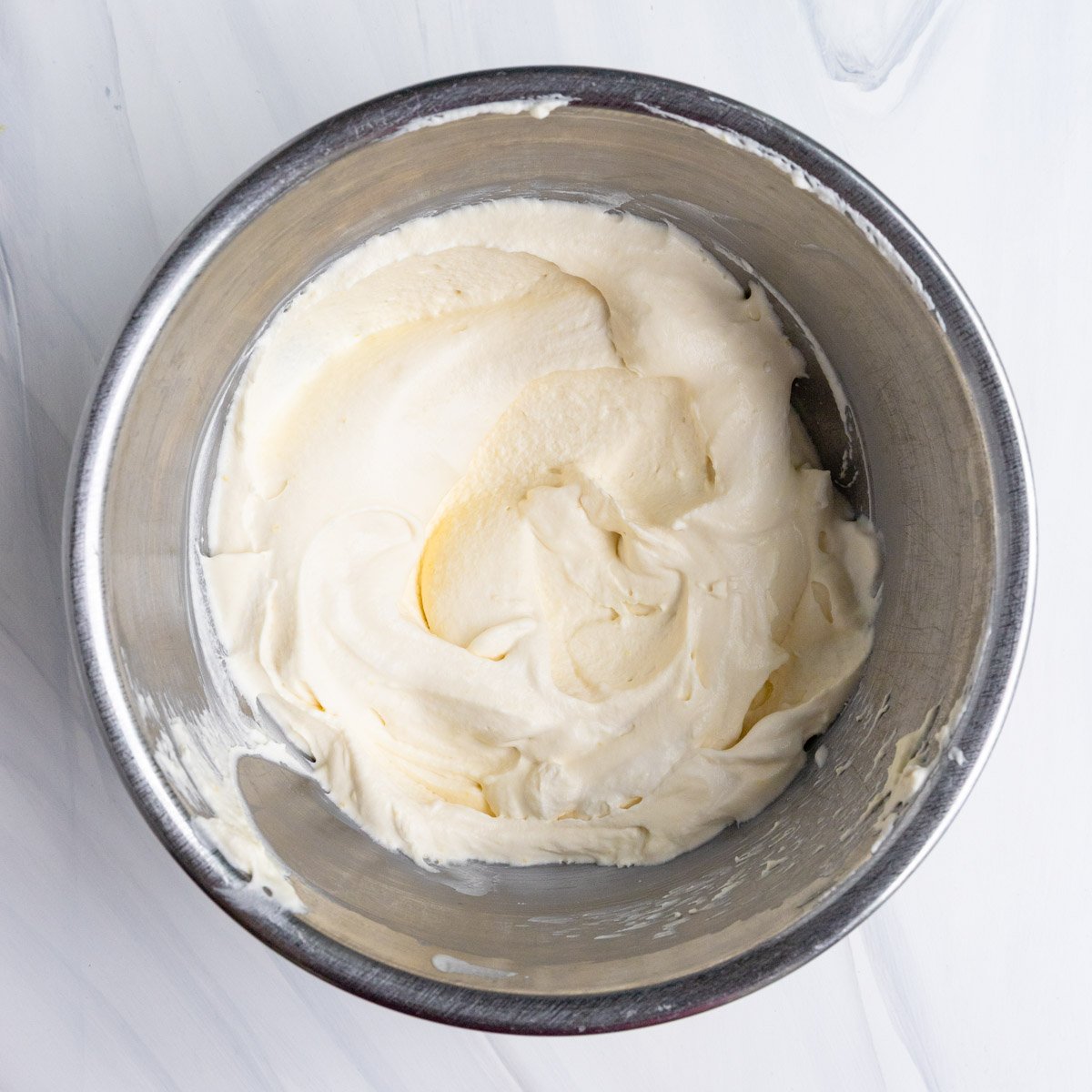 Whipped cream and lemon curd mixed together in a stainless steel bowl. The lemon cream is light yellow