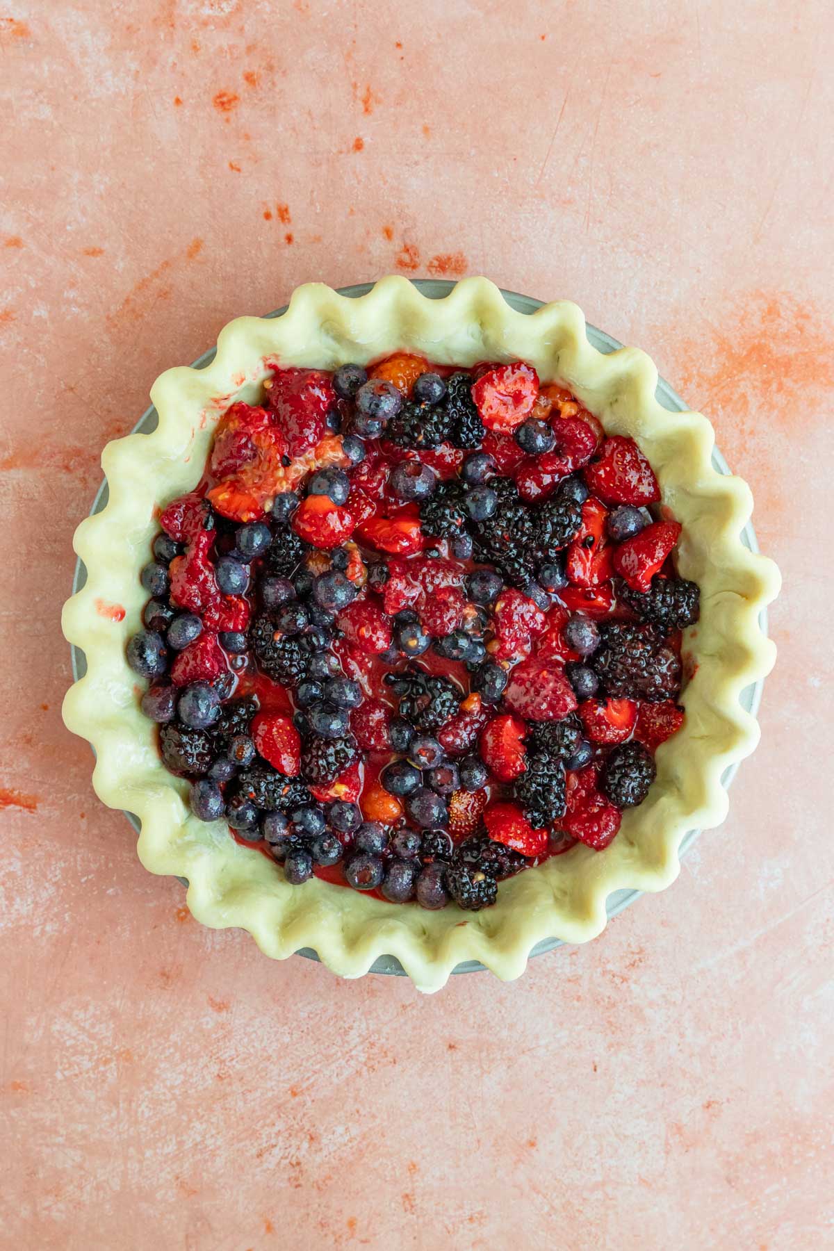 Pie dough in a pie plate filled with the mixed berry filling which is red, blue, and purple