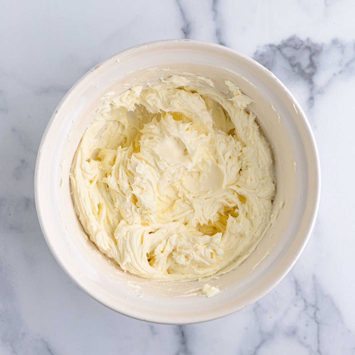 Whipped cream cheese, mascarpone cheese, and sugar in a large ceramic bowl.