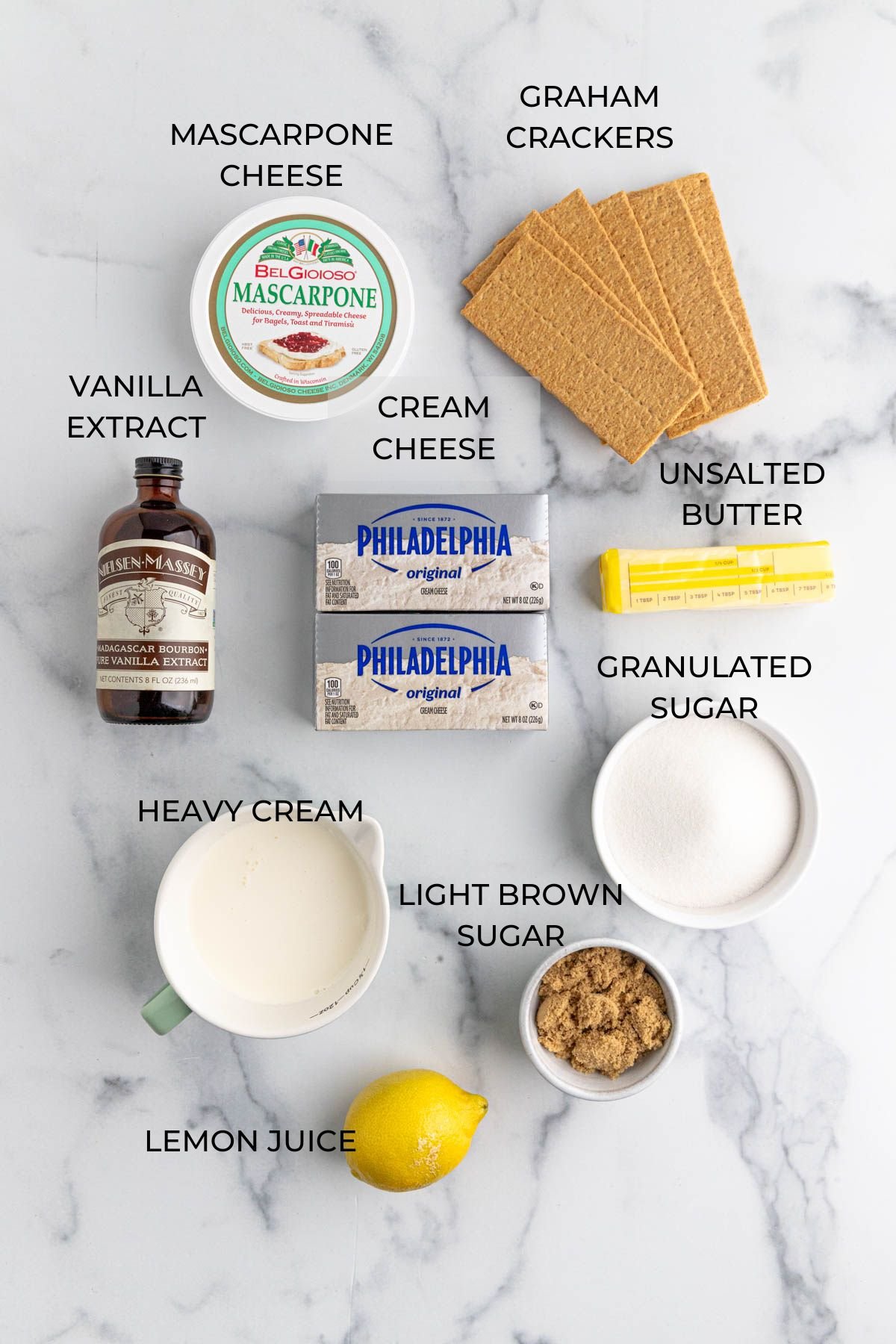 No Bake Cheese ingredients on a marbled surface: graham crackers, unsalted butter, granulated sugar, brown sugar, lemon juice, heavy cream, vanilla extra, cream cheese, mascarpone cheese.