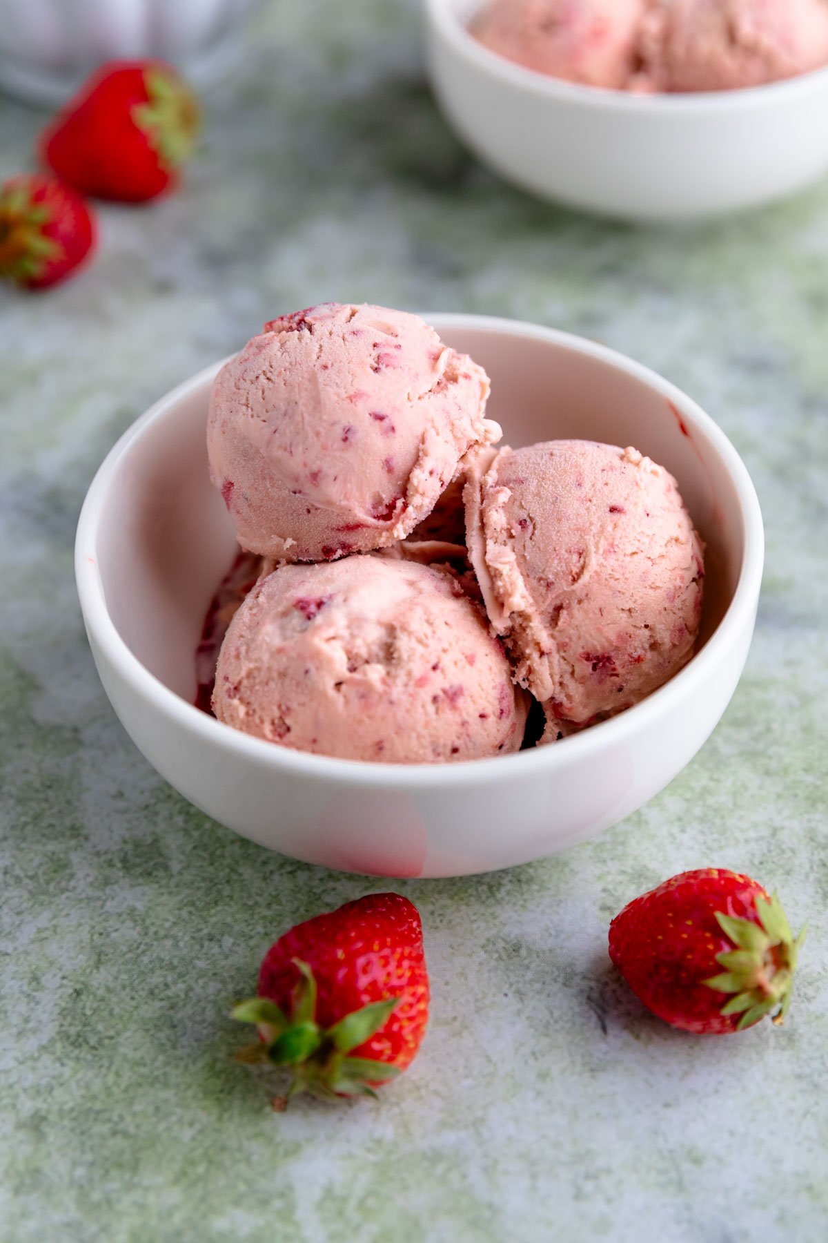 Three scoops of strawberry ice cream in a small white bowl